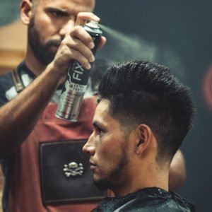 Experienced stylist applies finishing spray to clients hair during grooming session at modern barbershop.