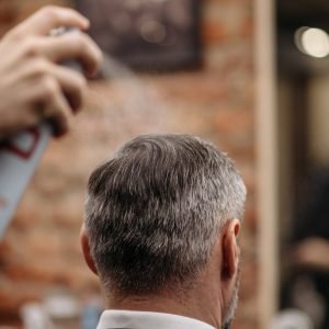 A professional barber styles a mans hair with hairspray in an urban barbershop.