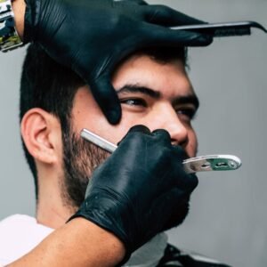 Servicios. Close-up of a barber shaving a mans beard with precision in a contemporary barbershop setting.